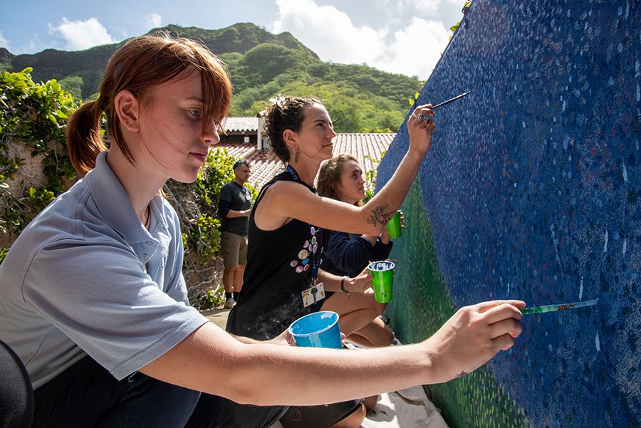 Students and teachers work together to paint a mural on campus.